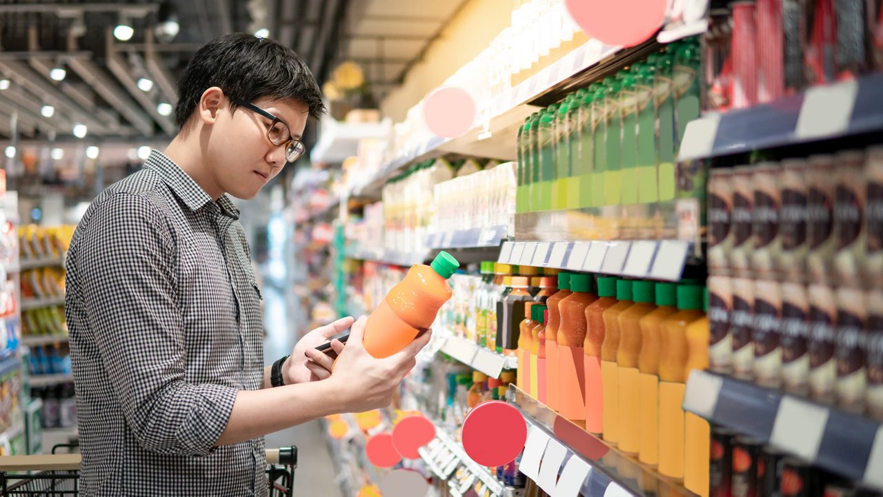 Young man wearing glasses holds and reads the label of bottled orange juice.