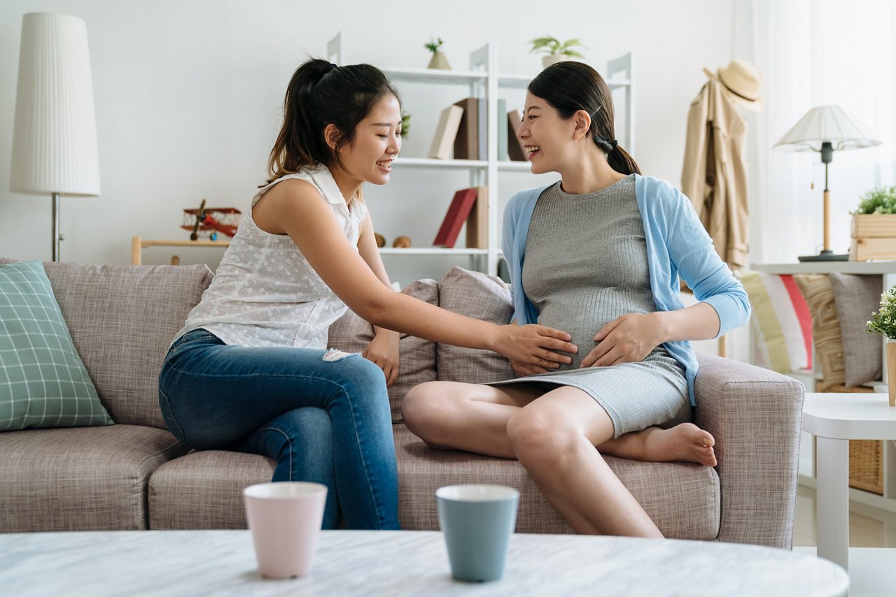 Woman presses her hand against her pregnant friend’s belly.