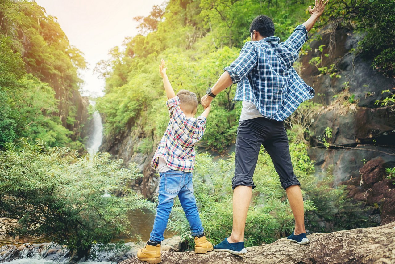 Father and son stand in a forest, raising their clasped hands in victory