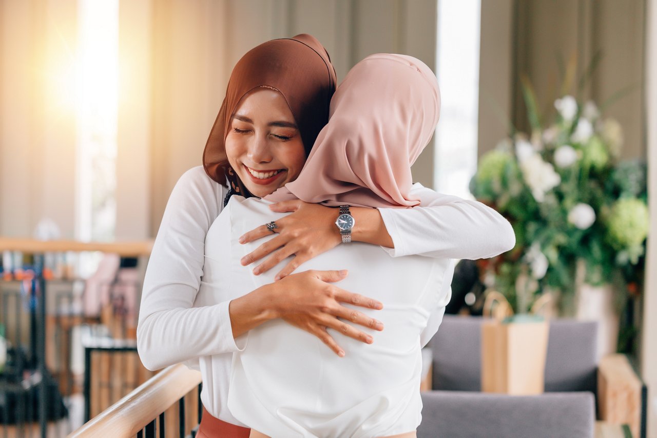 Two women wearing hijab hug each other.