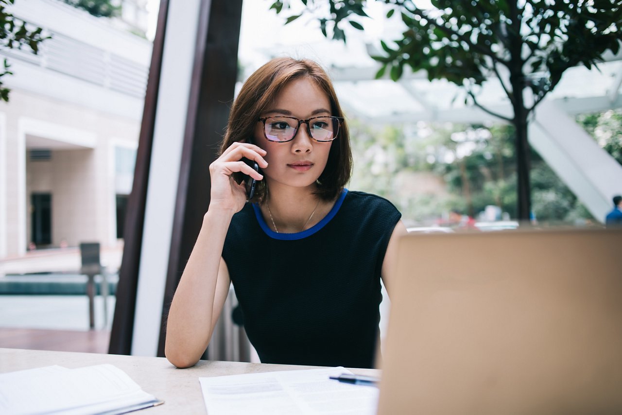 Young Asian woman on the phone stares at her laptop