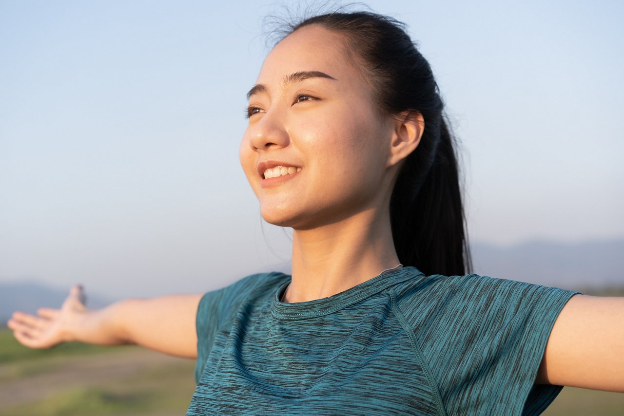 Smiling young woman spreads her arms at shoulder level to open up her chest.