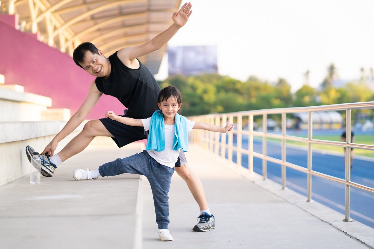 Father and young daughter perform a stretching exercise. 