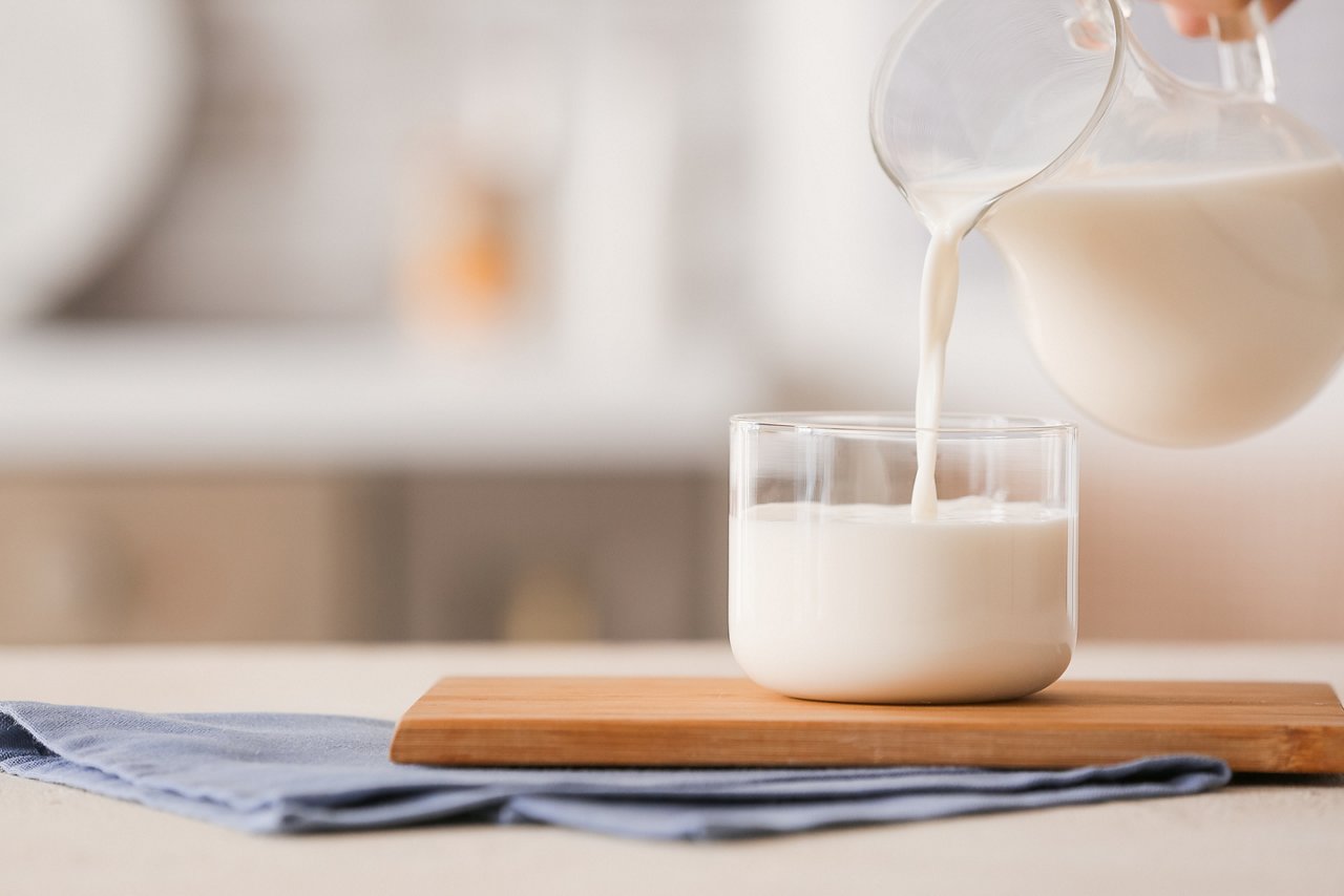 A hand pours a jug of milk into a glass on a table