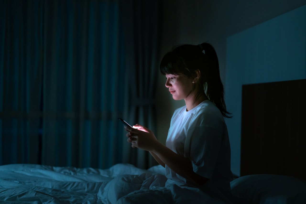 一位亞裔女性坐在床上看手機。 