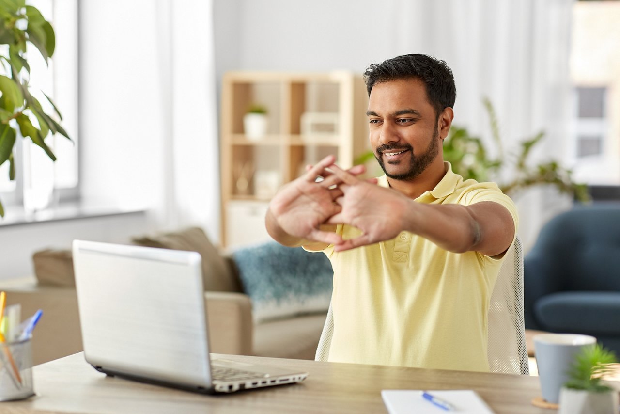 A man stretches his hands while sitting at his desk.