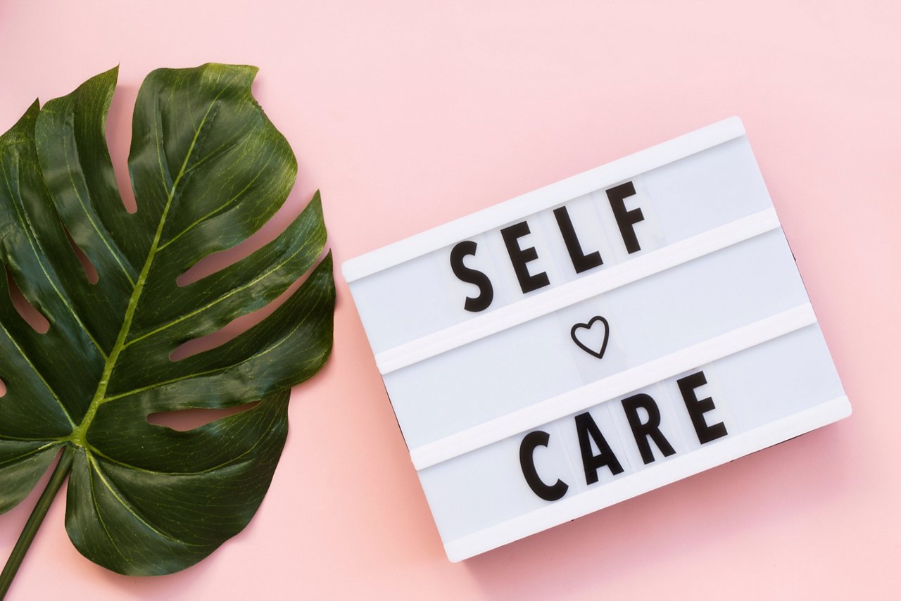 Flat lay of big plant leaf and lightbox with the word self-care against a pink background