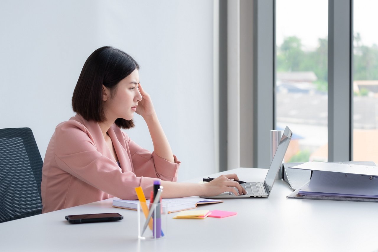 A young woman wearing a pink blazer looks worried in front of her laptop.