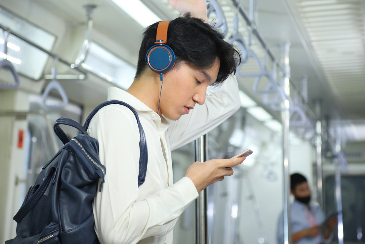 A young male with headphones looks at his mobile phone inside a train.
