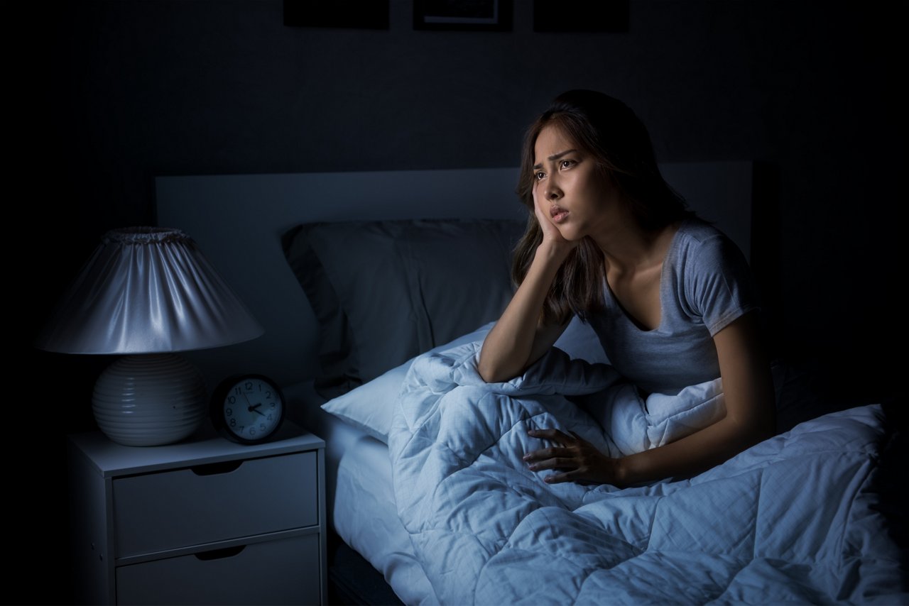 Depressed young Asian woman sitting in bed cannot sleep from insomnia