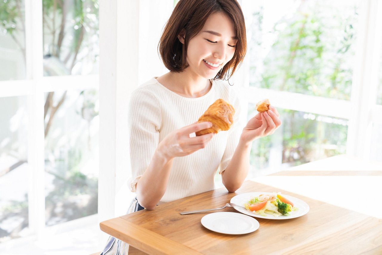 Asian woman eats a croissant and salad