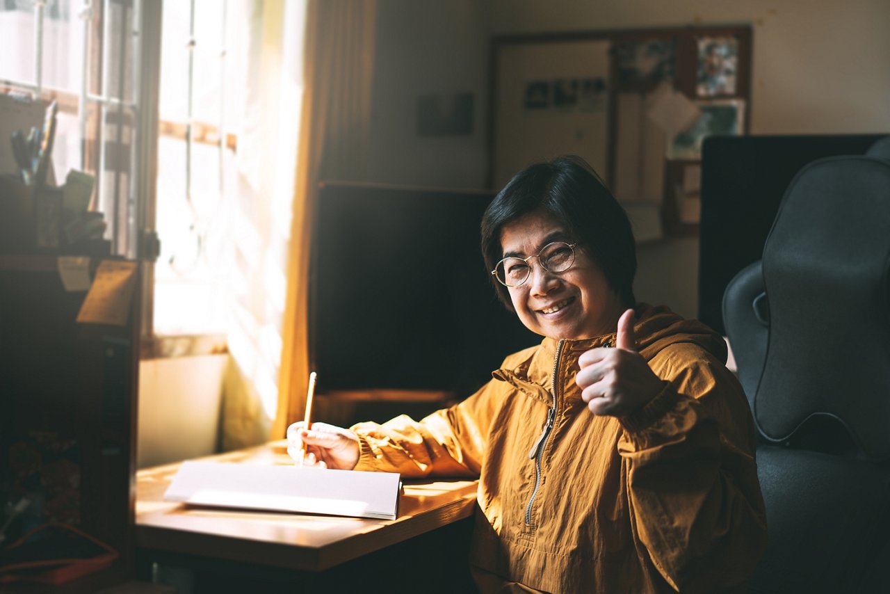 Elderly Asian woman gives a thumbs-up sign from her home office.