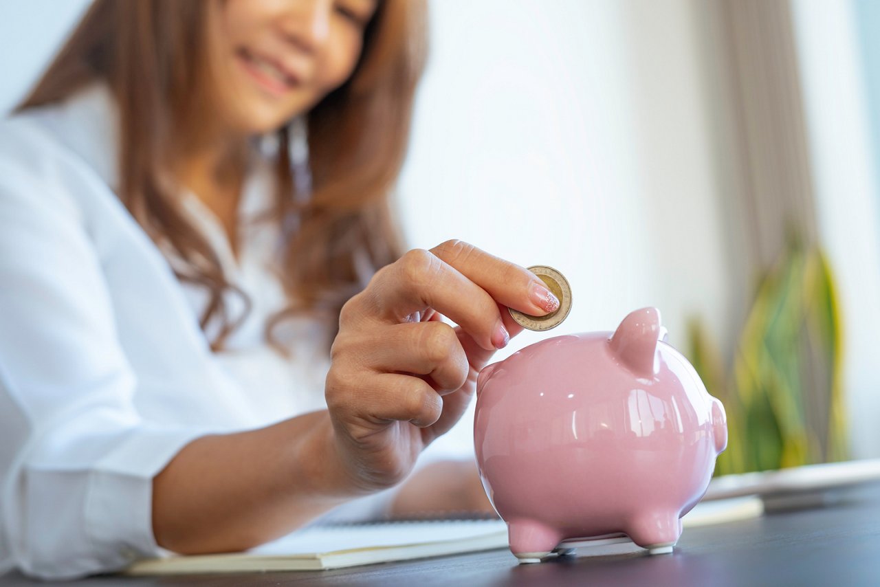 A woman drops a coin in a piggy bank.