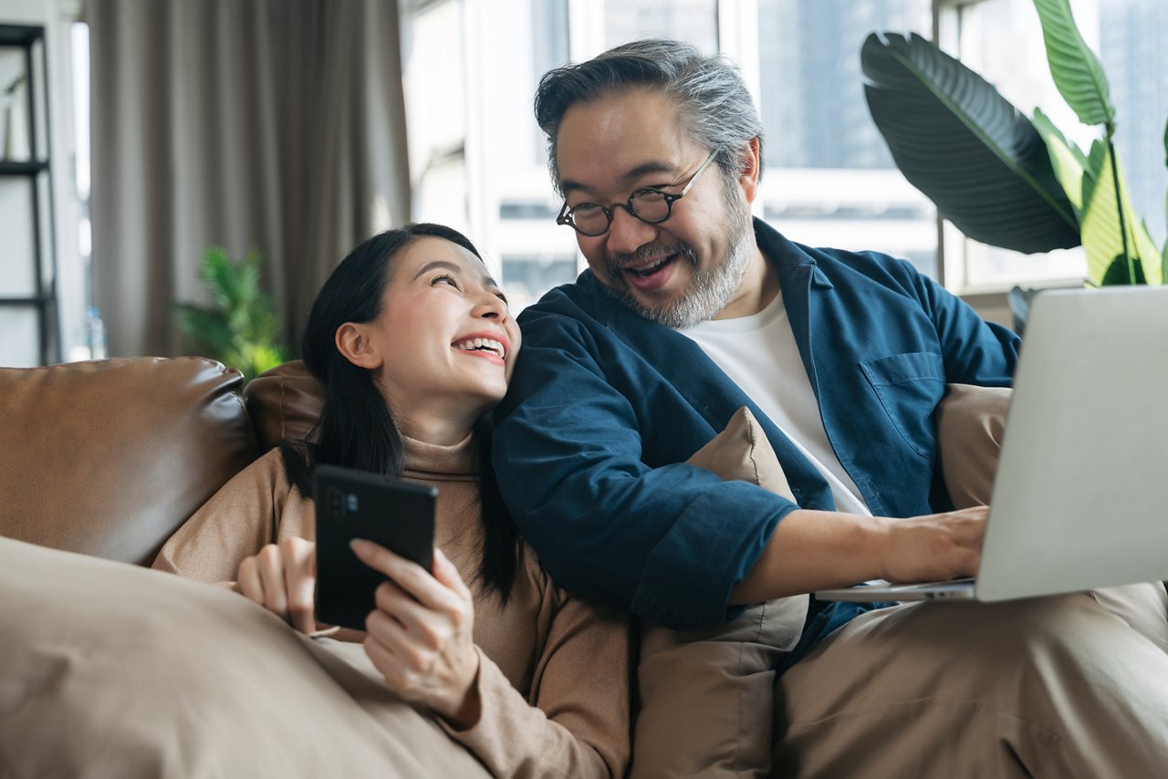 Young Asian couple looks at each other while holding gadgets.