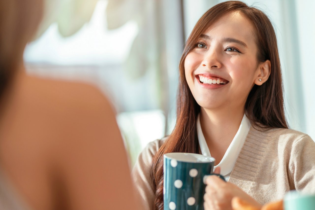 Young Asian woman holding a cup flashes a smile to her companion.