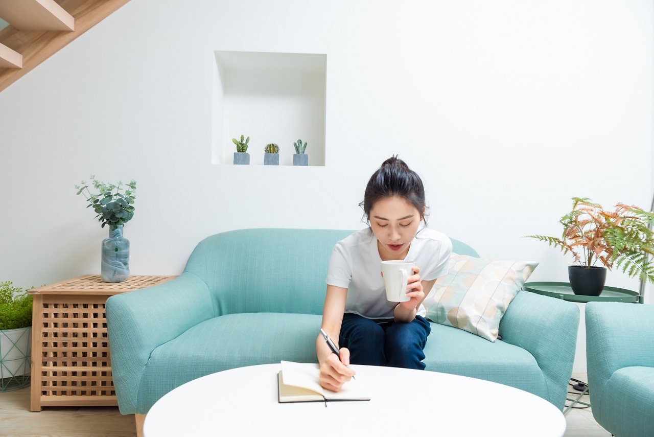 Young woman drinks coffee while writing in a notebook