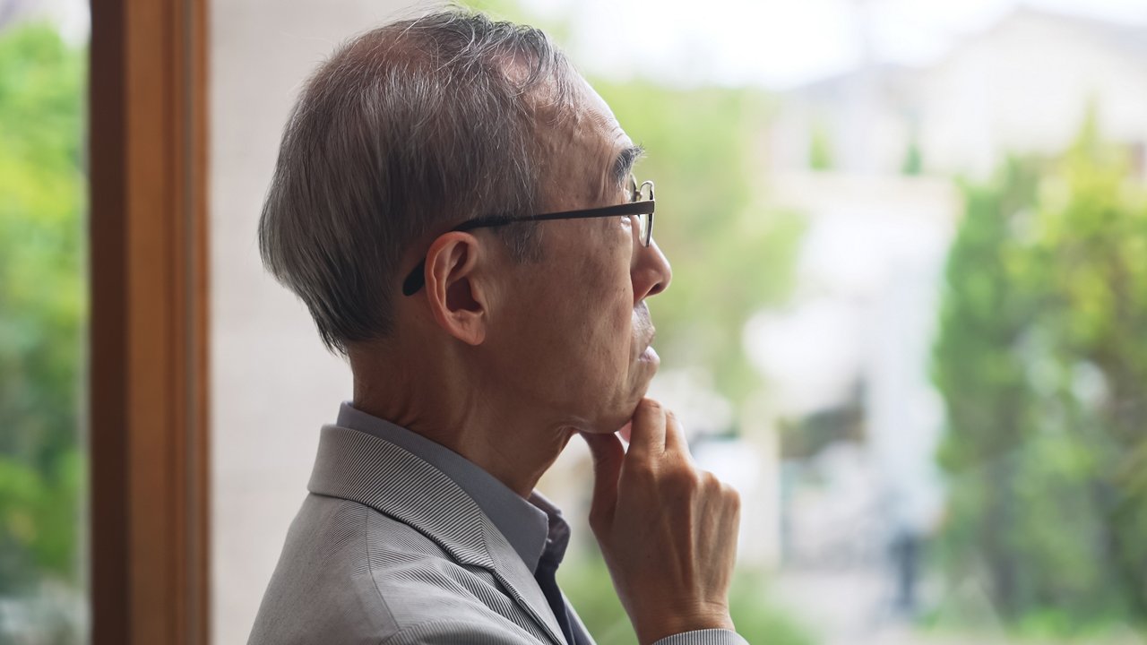 Senior Asian man stares out the window with a pensive look