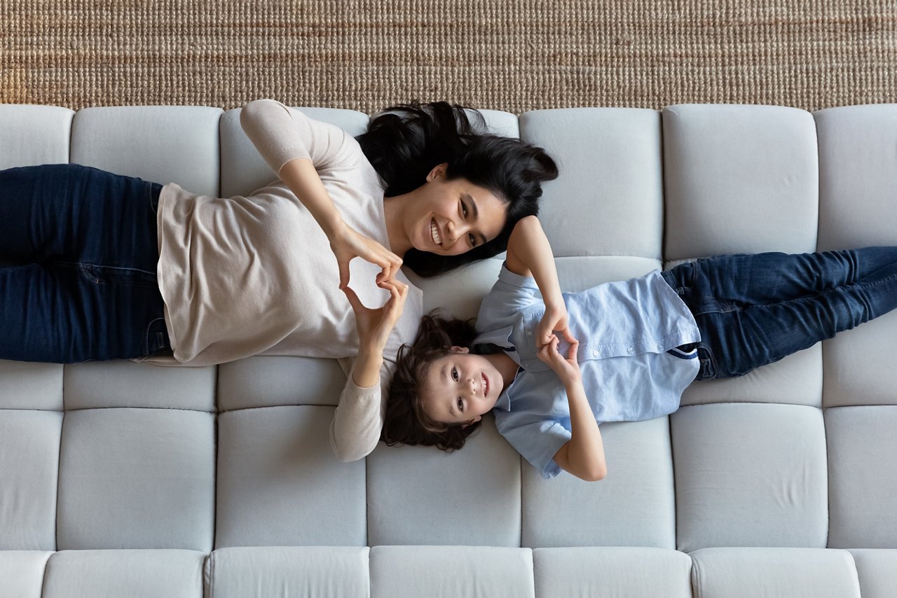 Top view image of a mother and her son lying on a couch making heart shapes with their fingers.