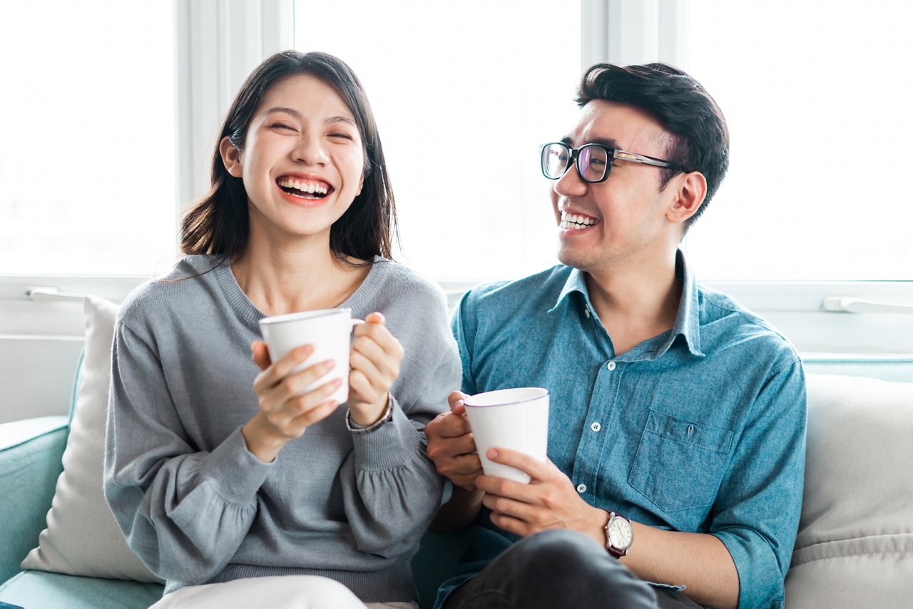 A man and woman laugh together as they drink from a cup.