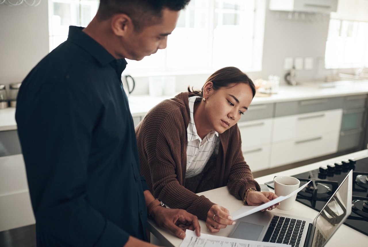 A couple looks at documents with a laptop open in the kitchen.