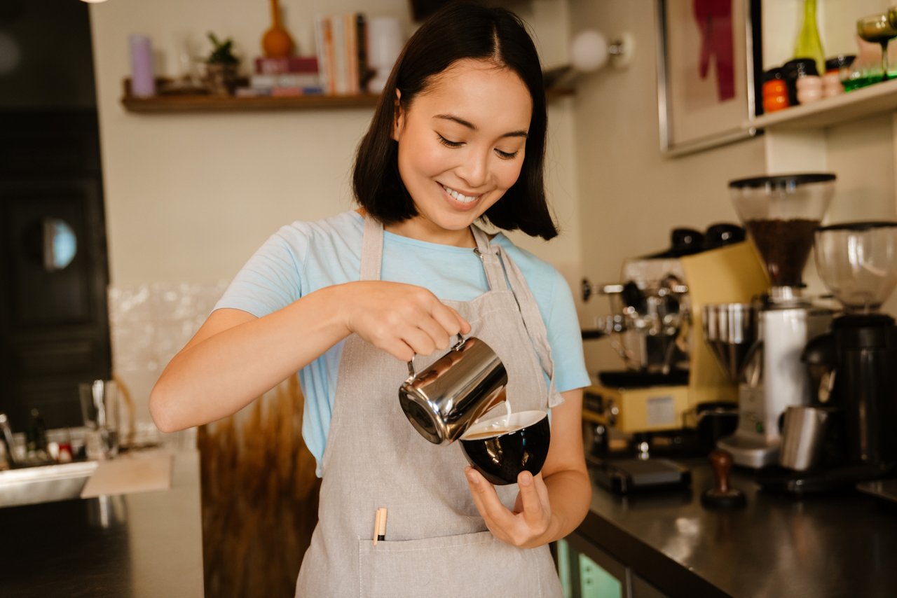 Young Asian barista woman smiling while making coffee in a cafe