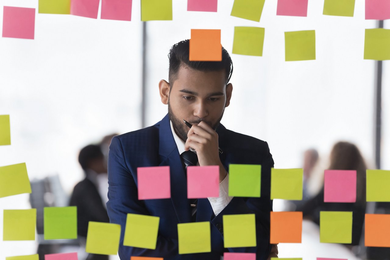 Man in corporate suit reviews post-it notes on a glass wall.