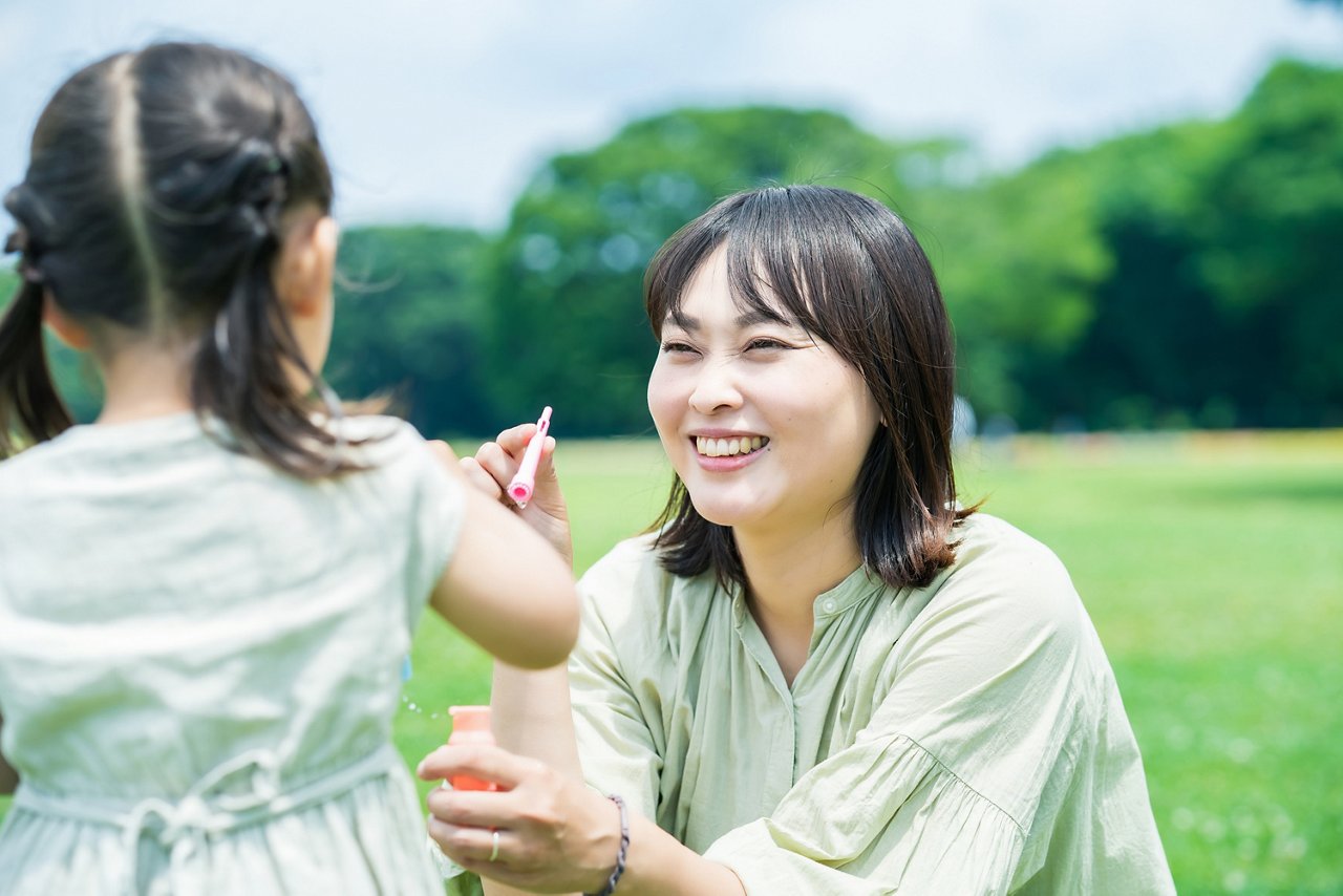 一位亞裔女性與女兒在公園裡玩泡泡機。 