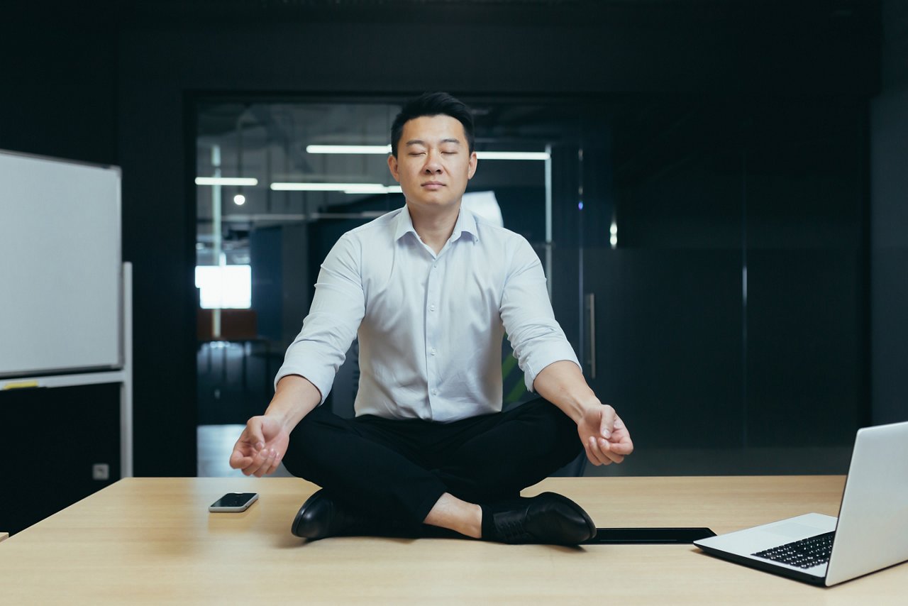 Asian businessman meditates on top of a desk