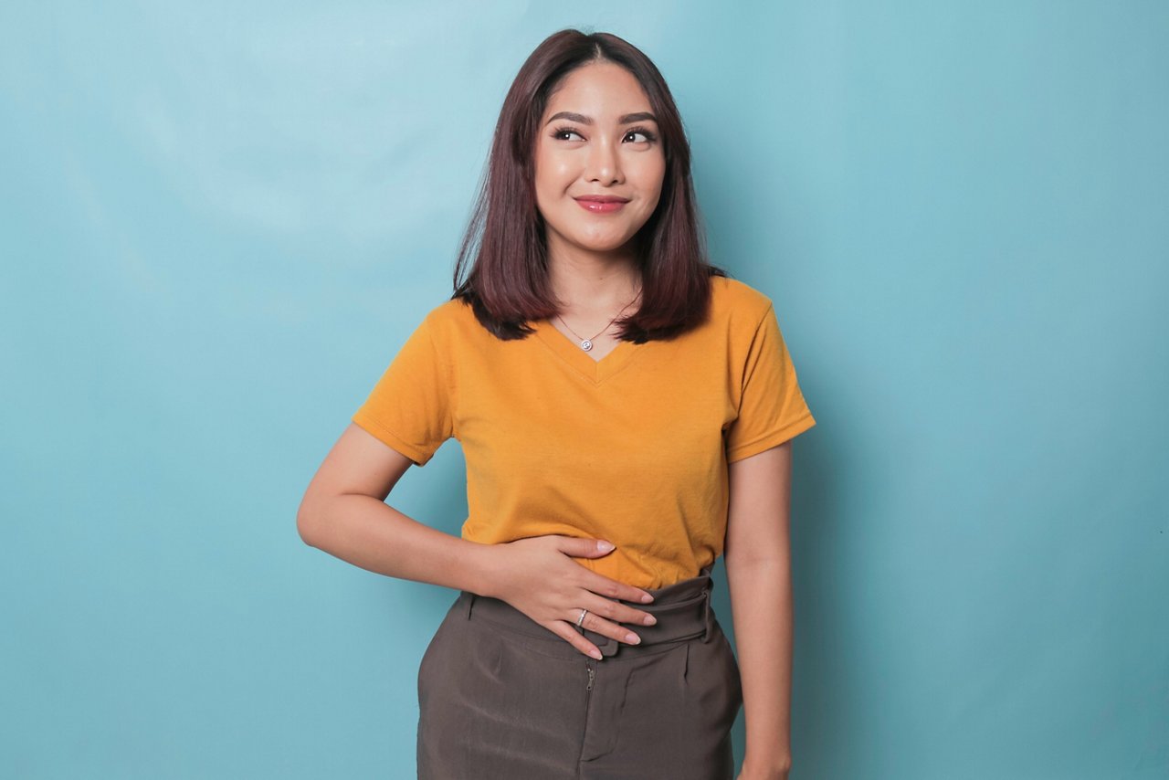 Smiling young woman with a sideways glance keeps her hand on her stomach.