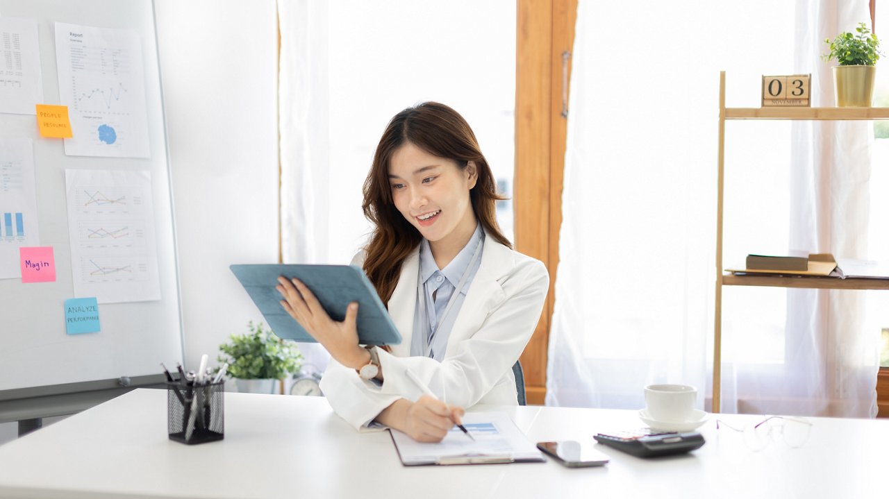 A young female business owner takes notes of transactions seen on her tablet