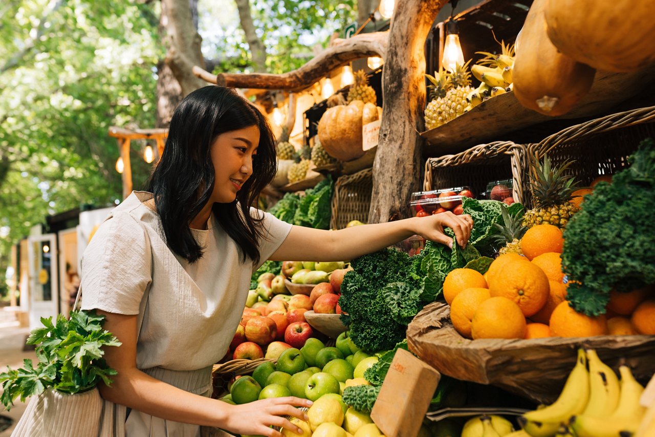 一位亞裔女性在農貿市場選購蔬菜和水果 