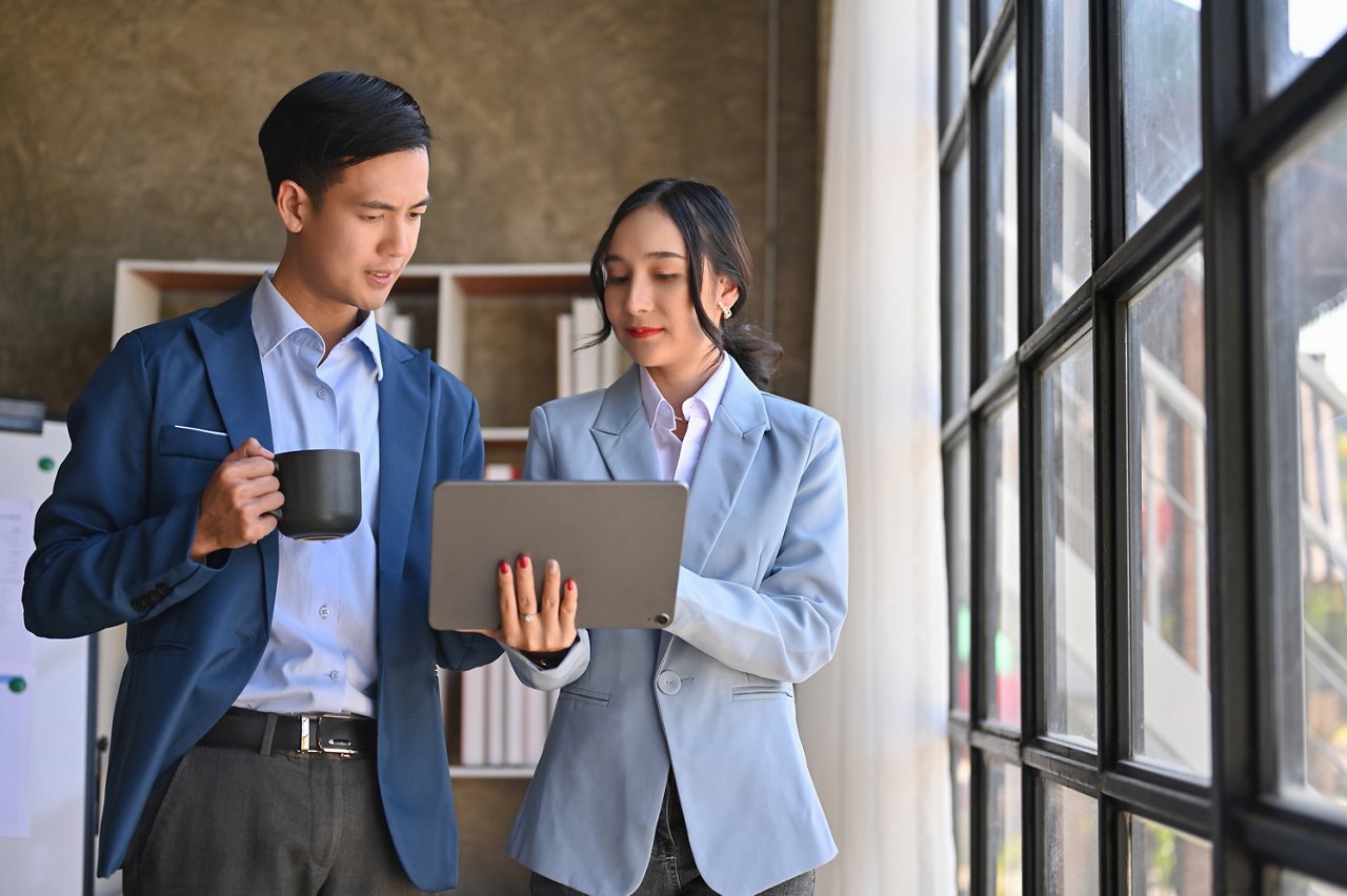 Male and female colleagues converse while looking at a tablet.