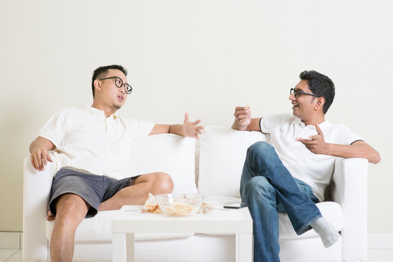 Two Asian men converse while sitting on a sofa.