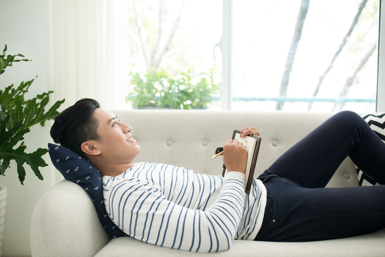 A man holds a journal while reclining on a sofa.