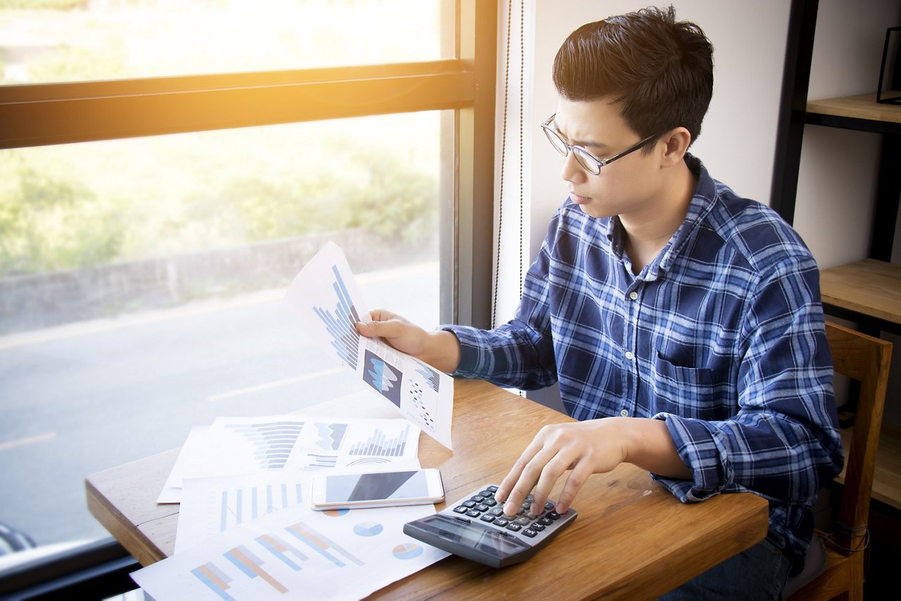 Young male Asian in his 30s uses a calculator while looking at charts