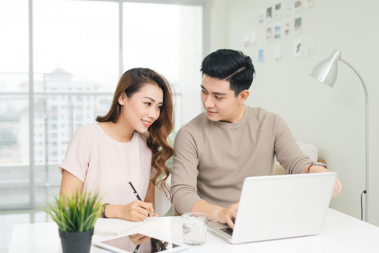 Happy young couple reading and analyzing bills sitting at table. Young couple in casual discussing home economics