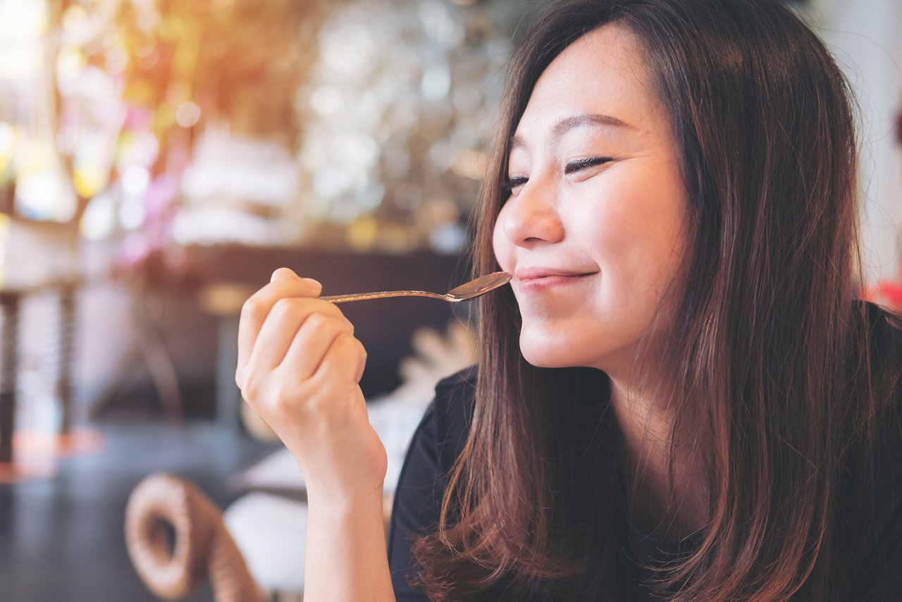 Young Asian woman smiles with her spoon in mid-air