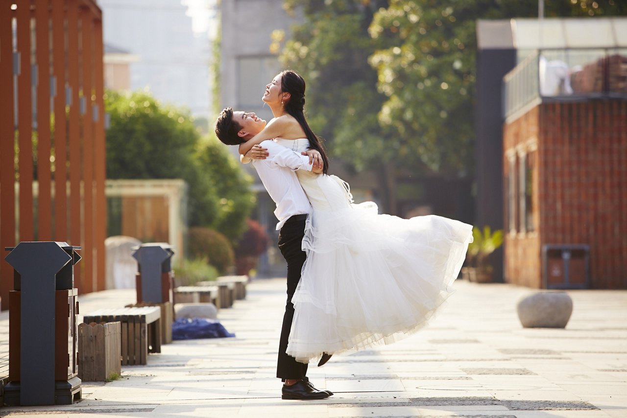 asian newly wed bride and groom celebrating marriage and hugging outside a building.