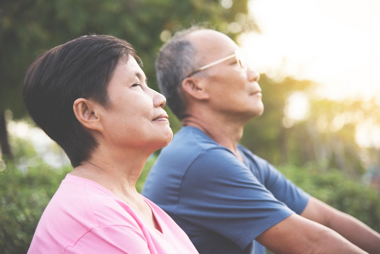 An elderly couple sits together and performs a breathing exercise