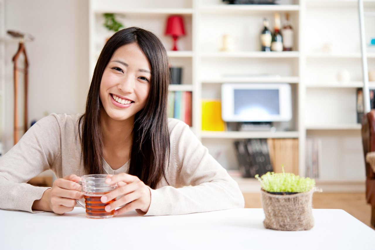Asian woman nurses a cup of tea at home.
