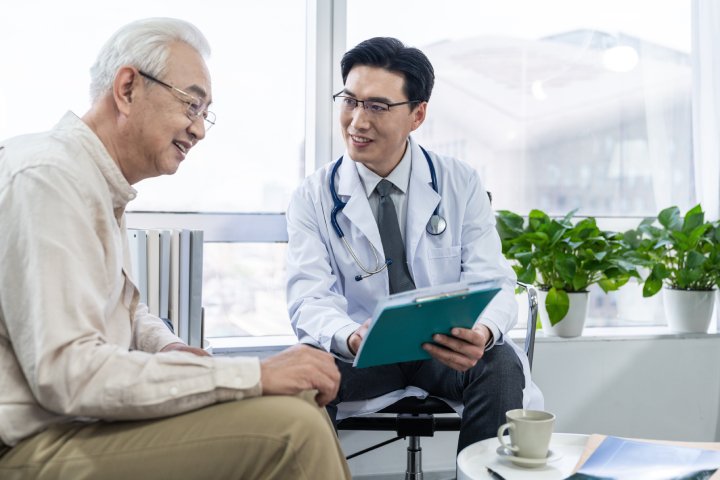Older man speaking with a doctor about stomach cancer symptoms, abdominal pain, digestive issues, and early warning signs.