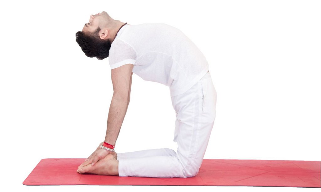Người đang thực hiện tư thế yoga trên thảm đỏ, tay chạm gót chân, thân uốn cong về phía sau.