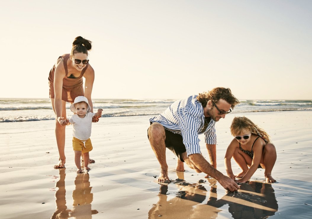 A family joyfully playing on the beach, engaging with their child in a sunny, vibrant seaside setting.