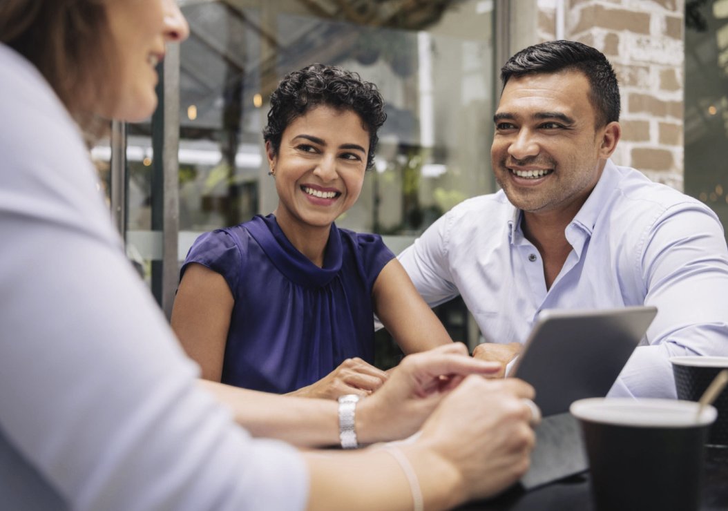 A man and woman are seated at a table, both engaged with a tablet in front of them, sharing ideas and collaborating.