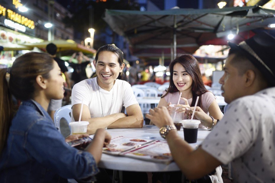 Four friends sitting around an outdoor restaurant table with drinks