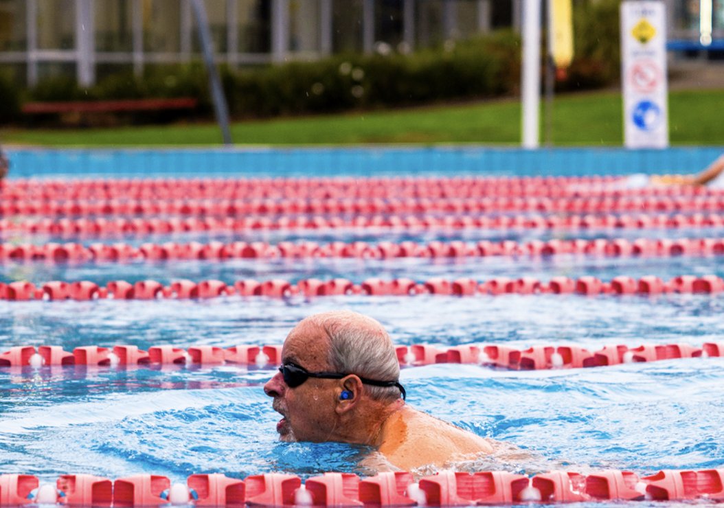 An older man swims gracefully in a clear blue pool, enjoying the refreshing water on a sunny day.