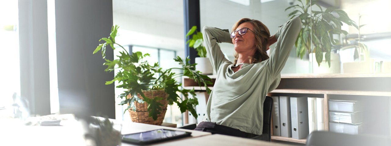 A woman at her desk, sitting in front of a computer with her arms raised enthusiastically.