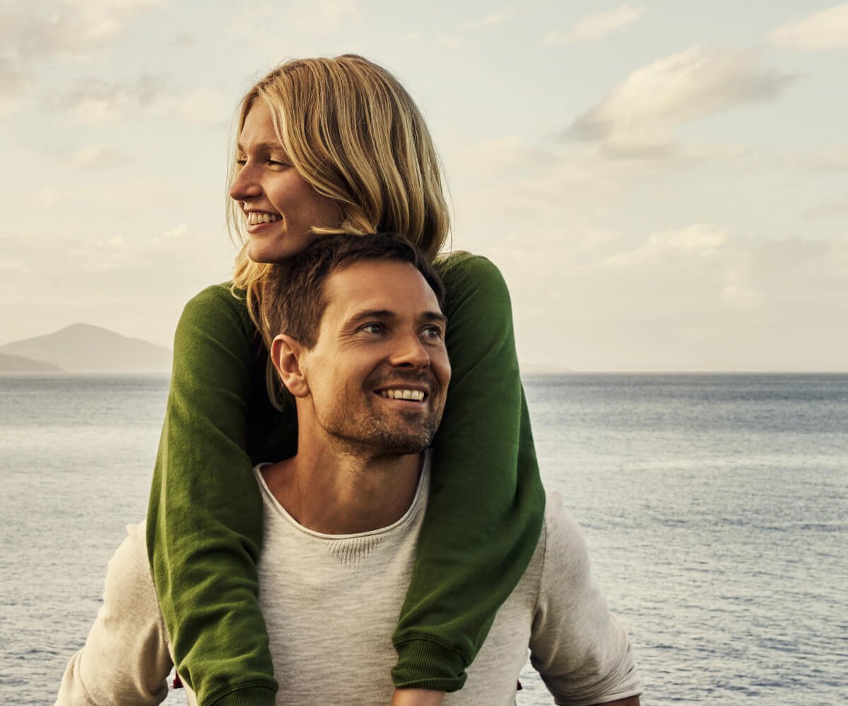 A couple stands on the beach, holding each other closely as they enjoy the serene ocean view.