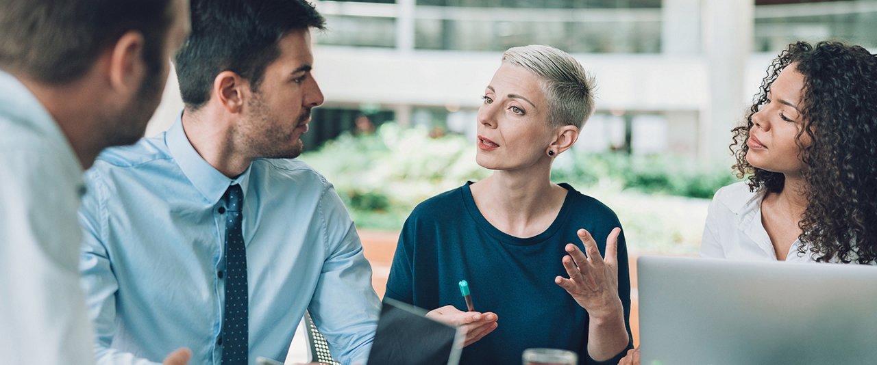 Three business professionals engaged in discussion around a conference table, sharing ideas and strategies.