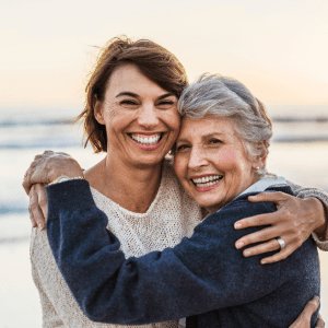 A woman embracing her elderly mother in a hug at the beach